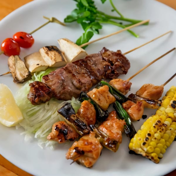 A white plate with various Japanese yakitori skewers, including meat, mushrooms, and corn, with a lemon wedge.