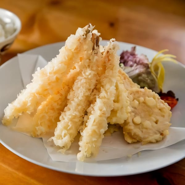 Crispy golden tempura shrimp and vegetables on a white plate with a lemon wedge.