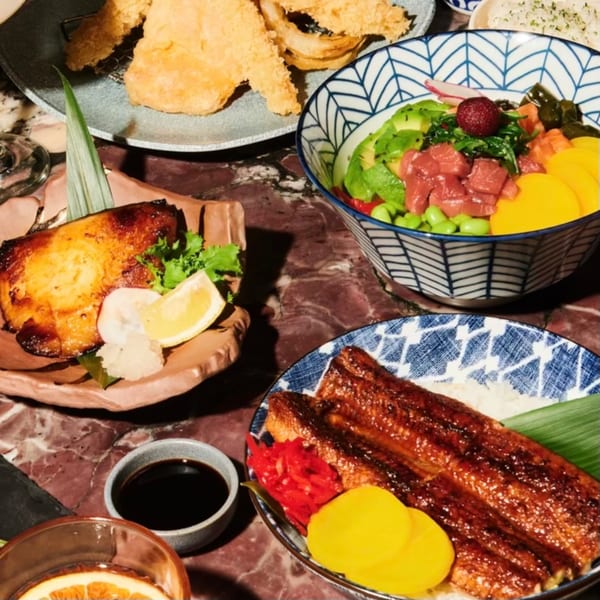 A variety of Japanese dishes, including grilled fish, poke bowl, and unagi, on a marble table.