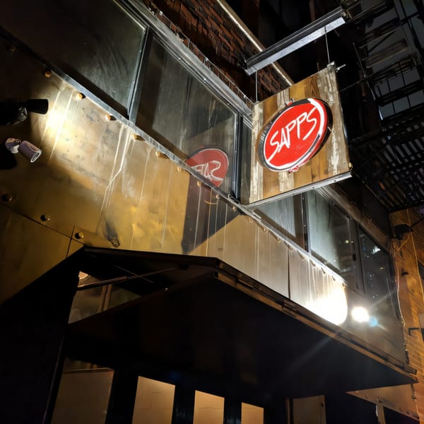 The Sapps NYC restaurant exterior at night, with a red circular sign and warm lighting.