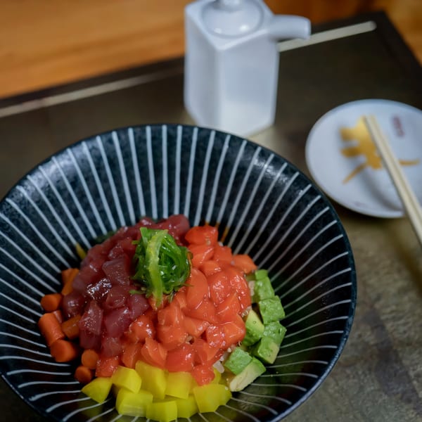 Colorful poke bowl with tuna, salmon, avocado, and pickled vegetables, with chopsticks and soy sauce.
