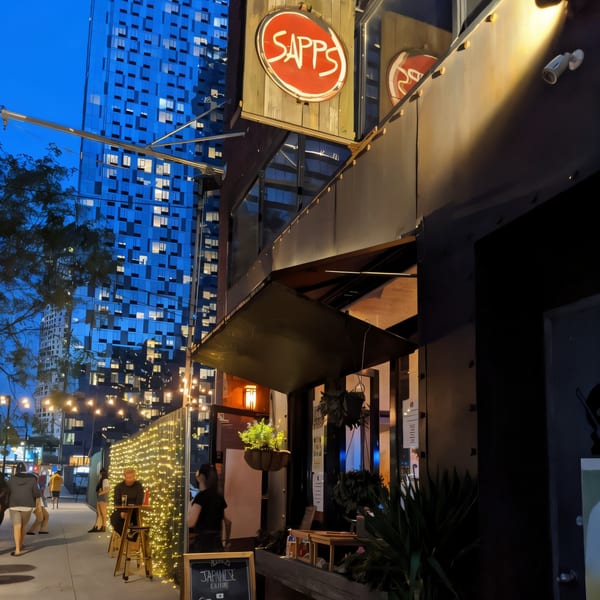 Sapps Nyc Japanese restaurant exterior at dusk with string lights and a blue high-rise building.