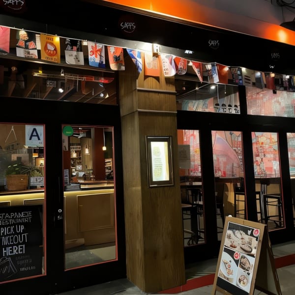 Sapps Nyc Japanese restaurant exterior at night, with colorful banners, a menu display, and a sandwich board.